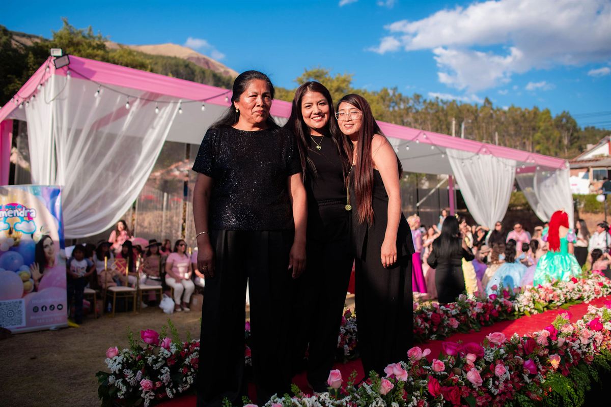 Tres mujeres vestidas de negro sonríen junto a la pasarela con flores, durante el lanzamiento de la colección